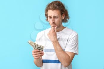 Thoughtful young man with dollar banknotes on color background�