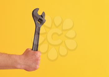 Hand of plumber with wrench on color background�
