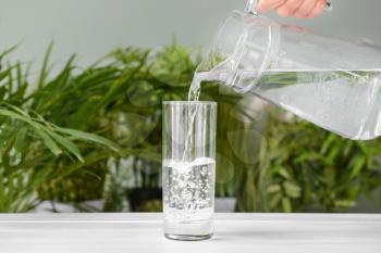 Pouring of fresh water into glass on table�