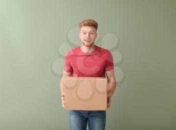 Young man with cardboard box on color background�