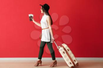 Going young woman with suitcase, passport and ticket near color wall�