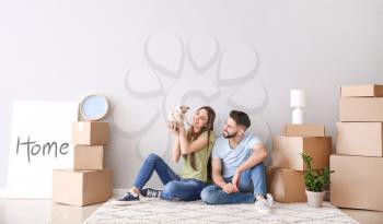 Young couple with belongings and kitten sitting near light wall in their new house�
