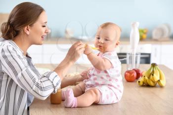 Mother feeding her little baby in kitchen at home�