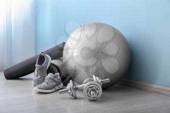 Set of sports equipment with fitness ball and shoes near color wall�
