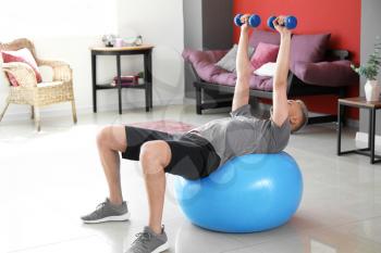 Young man doing exercise with fitball and dumbbells at home�