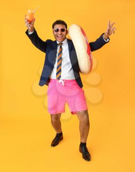 Funny office worker with cocktail and swimming ring dreaming about vacation on color background�