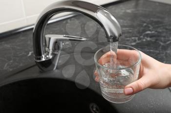 Woman filling glass with water from kitchen faucet�