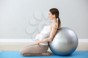 Beautiful pregnant woman with fitball training near grey wall�