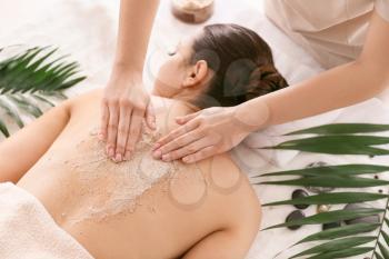Young woman undergoing treatment with body scrub in spa salon�