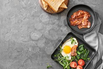 Composition with tasty fried egg and bacon on grey background�