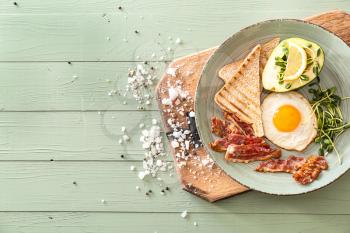 Plate with tasty fried egg, bacon, avocado and toasts on table�