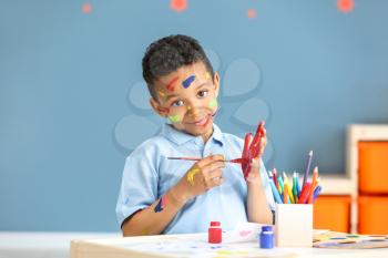 Cute African-American boy with hands and face in paint at home�