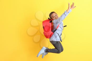 Jumping African-American schoolboy on color background�