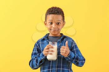 Cute African-American boy with glass of milk showing thumb-up on color background�