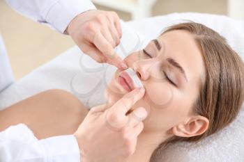 Beautician removing hair above upper lip of young woman in salon�
