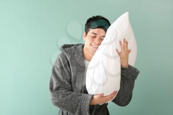 Handsome young man with sleep mask and pillow on color background�