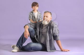 Cute little boy with grandfather on color background�