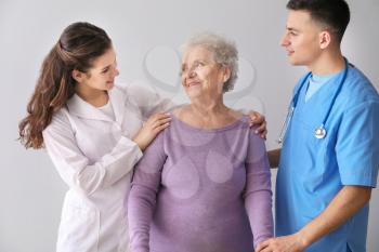 Young medical workers with senior woman on grey background 