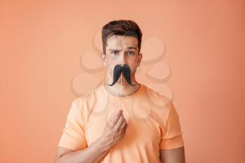 Funny portrait of handsome man with fake mustache on color background�