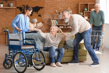 Caregiver and elderly man helping senior woman to sit in wheelchair 