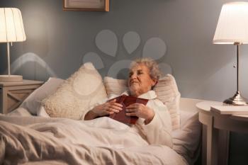 Senior woman with book sleeping in bed at night�