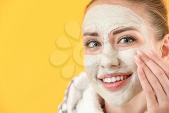 Beautiful young woman with facial mask on color background�