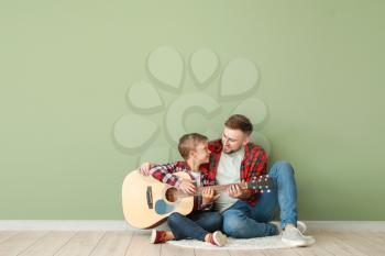 Portrait of happy father and son with guitar sitting near color wall�