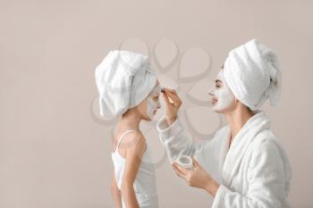 Mother applying cream onto face of her little daughter against grey background�