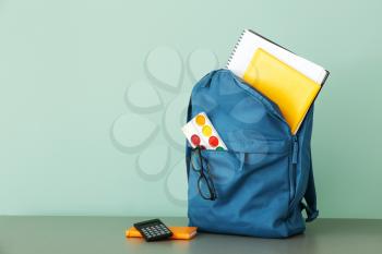 School backpack with stationery on table against color background�