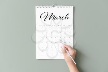 Woman marking date in calendar on color background�