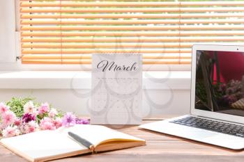 Calendar with laptop, flowers and stationery on table near window�
