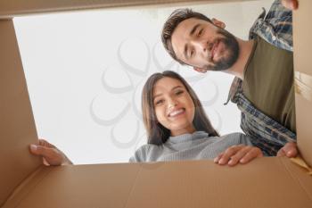 Young couple looking inside of cardboard box with belongings after moving into new house�