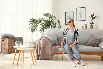 Young blind woman sitting on sofa at home�