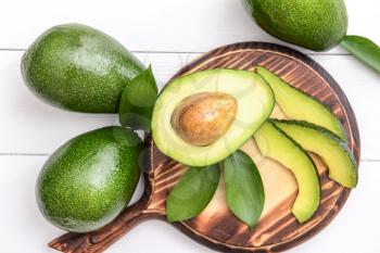 Board with fresh ripe avocados on white wooden background�