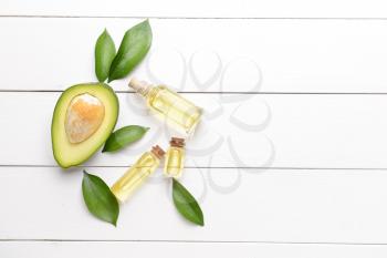 Fresh ripe avocados with essential oil on white wooden background�