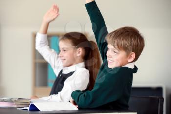 Cute little children raising hands during lesson in classroom�