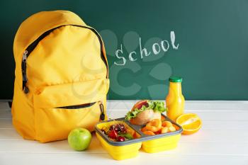 School lunch box with tasty food and backpack on table in classroom�