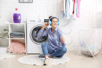 Beautiful young woman listening to music while doing laundry at home�