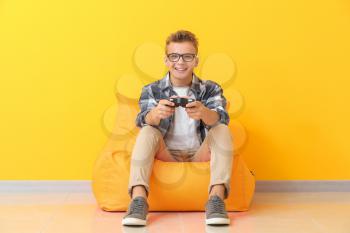 Teenage boy playing video game near color wall�