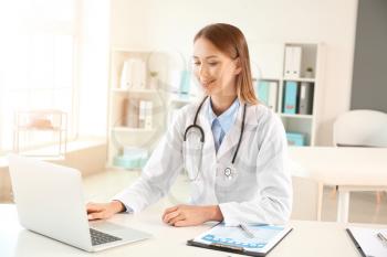 Female doctor working with laptop at table in clinic�
