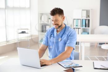 Male nurse working on laptop in clinic�