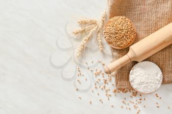Rolling pin with wheat grains and flour on light background�