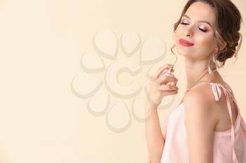 Beautiful young woman with bottle of perfume on light color background�