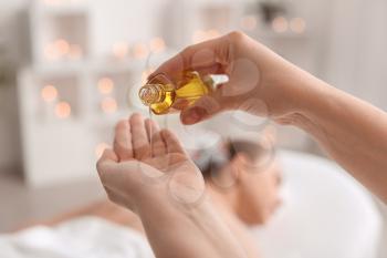 Massage therapist pouring essential oil onto hand in spa salon�