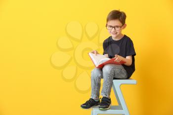 Little boy reading book on color background�