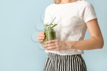 Young woman with tasty smoothie in mason jar on color background, closeup�