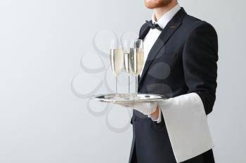 Handsome waiter with champagne on light background�
