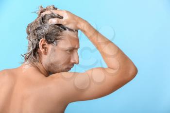 Handsome young man washing hair against color background�