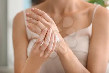 Young woman applying natural cream onto skin at home�
