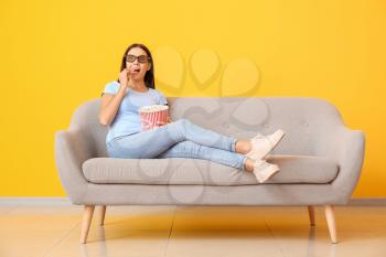 Young woman with popcorn watching movie on sofa near color wall�